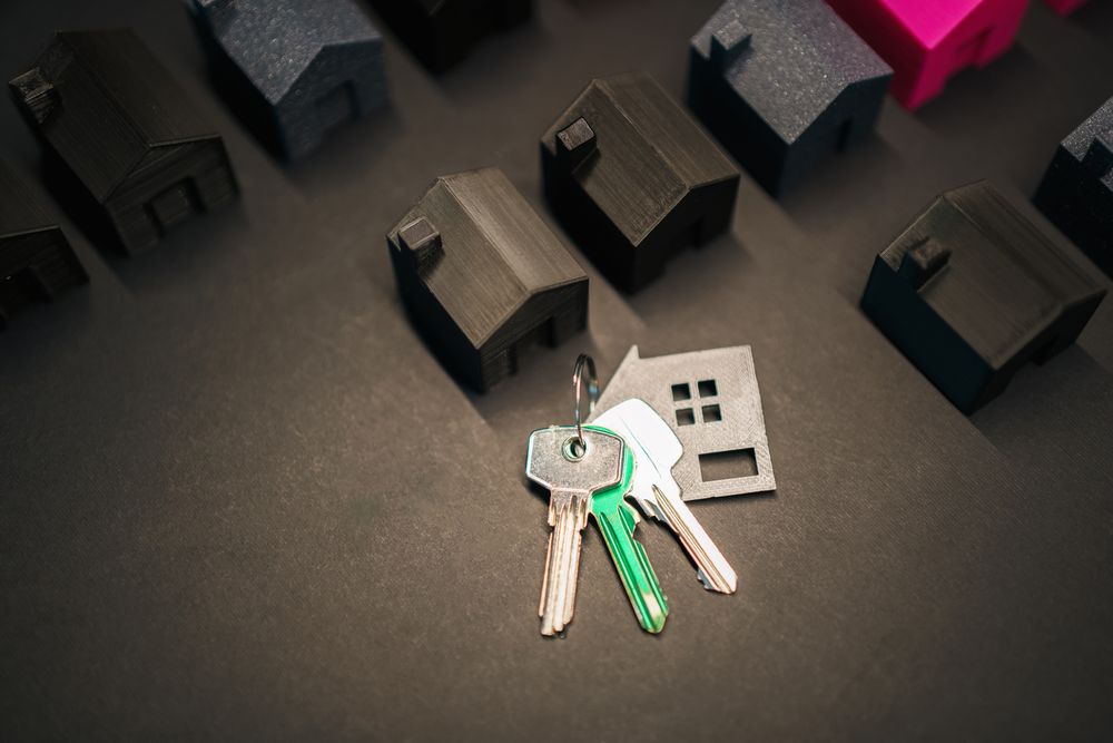 Tre nøgler og en lille husformet nøglering blandt miniaturehuse på en mørk flade