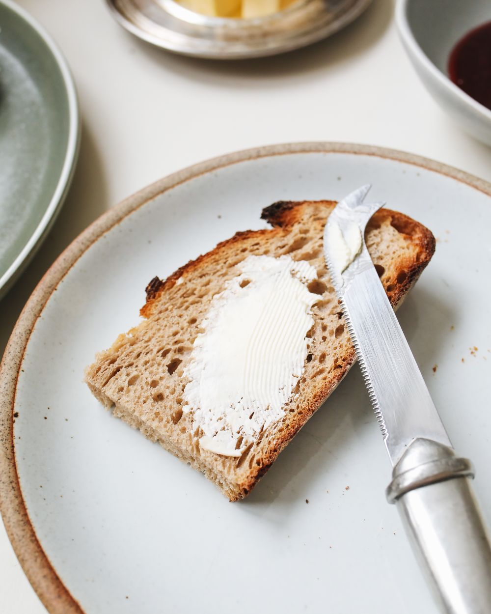 Skive brød med smør på en keramiktallerken med en smørkniv