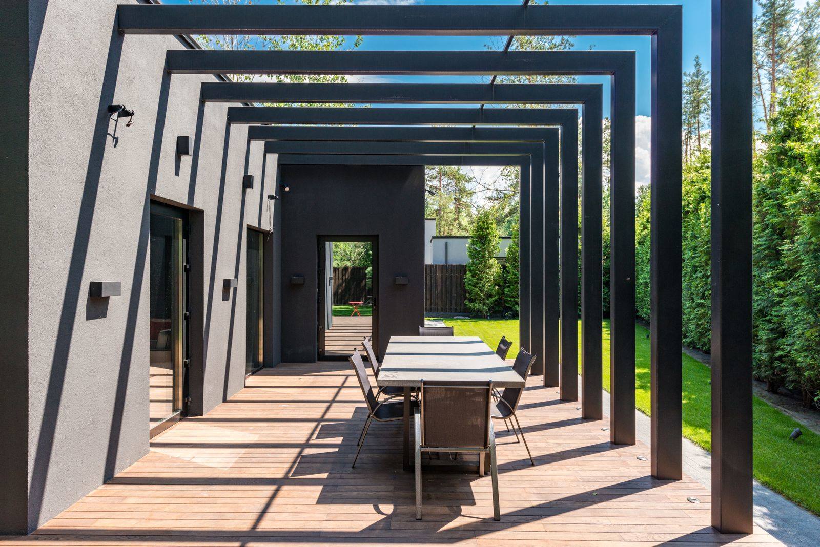Overdækket terrasse med spisebord under en pergola af sorte bjælker